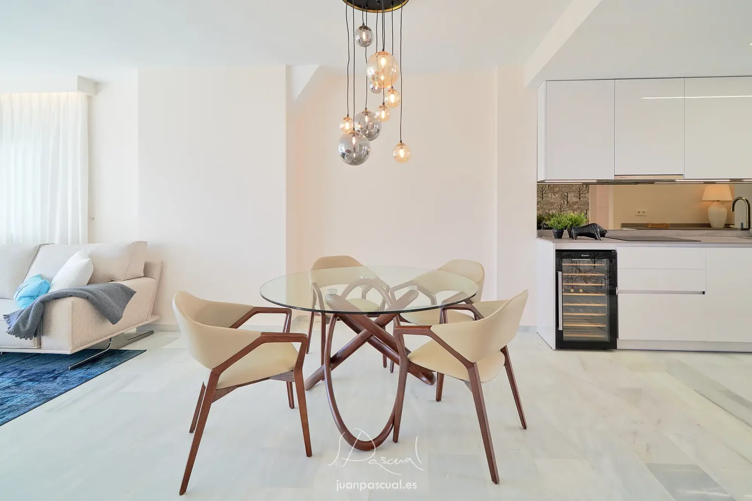 Fotografía del salón de un apartamento en Marbella, hecha por el fotógrafo inmobiliario Juan Pascual. Cocina integrada en el salón. Diseño moderno. Destaca la originalidad de la mesa central.
