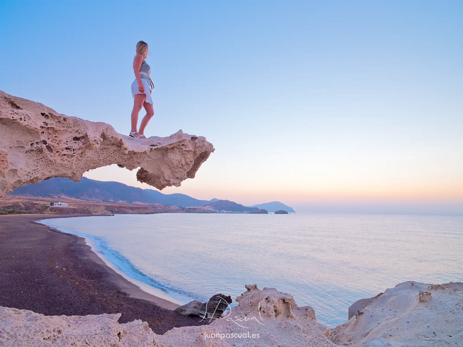 Fotografía de Cabo de Gata al amanecer por el fotógrafo de turismo Juan Pascual. Modelo rubia mira hacia la salida del sol en la playa de los Escullos.