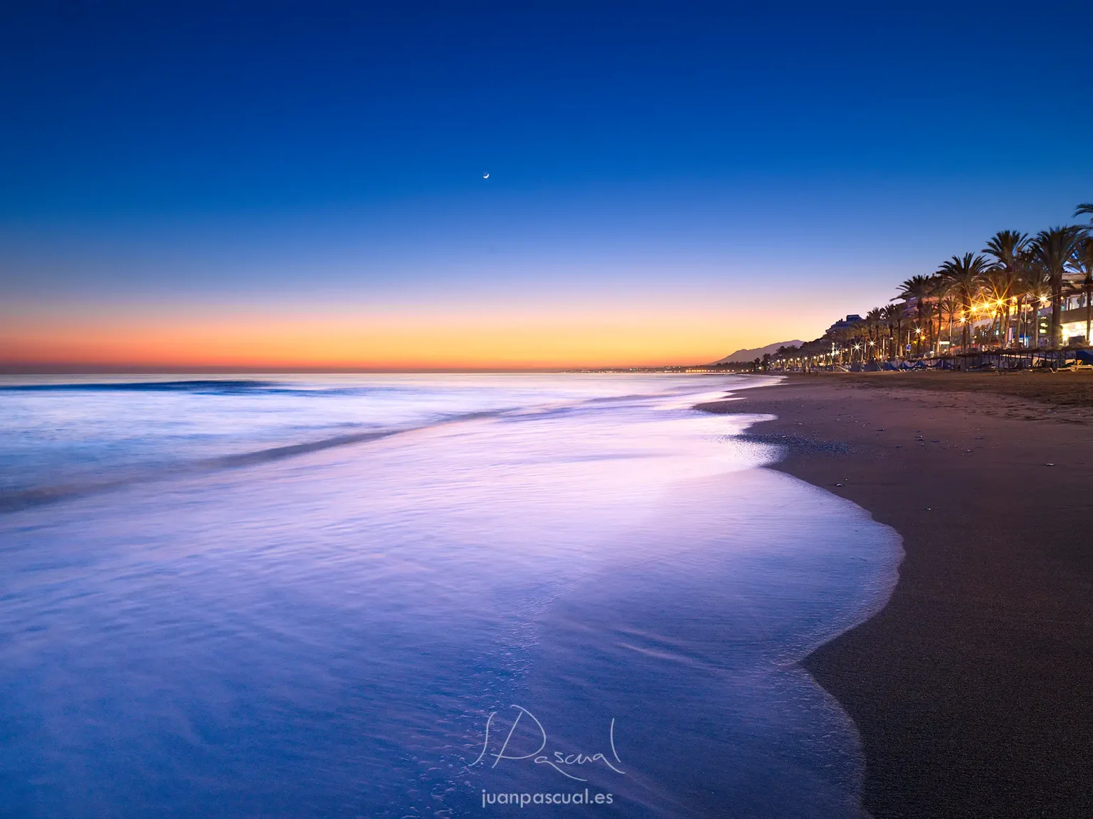 Última luz natural después de la puesta de sol en playa de Marbella, por el fotógrafo de turismo Juan Pascual. Suave oleaje. Tonos azules y naranjas.