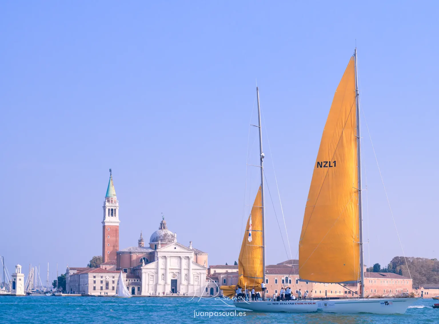 Fotografía de Venecia con velero de competición. Iglesia y embarcaciones atracadas en isla al fondo. Obra del fotógrafo de turismo Juan Pascual.