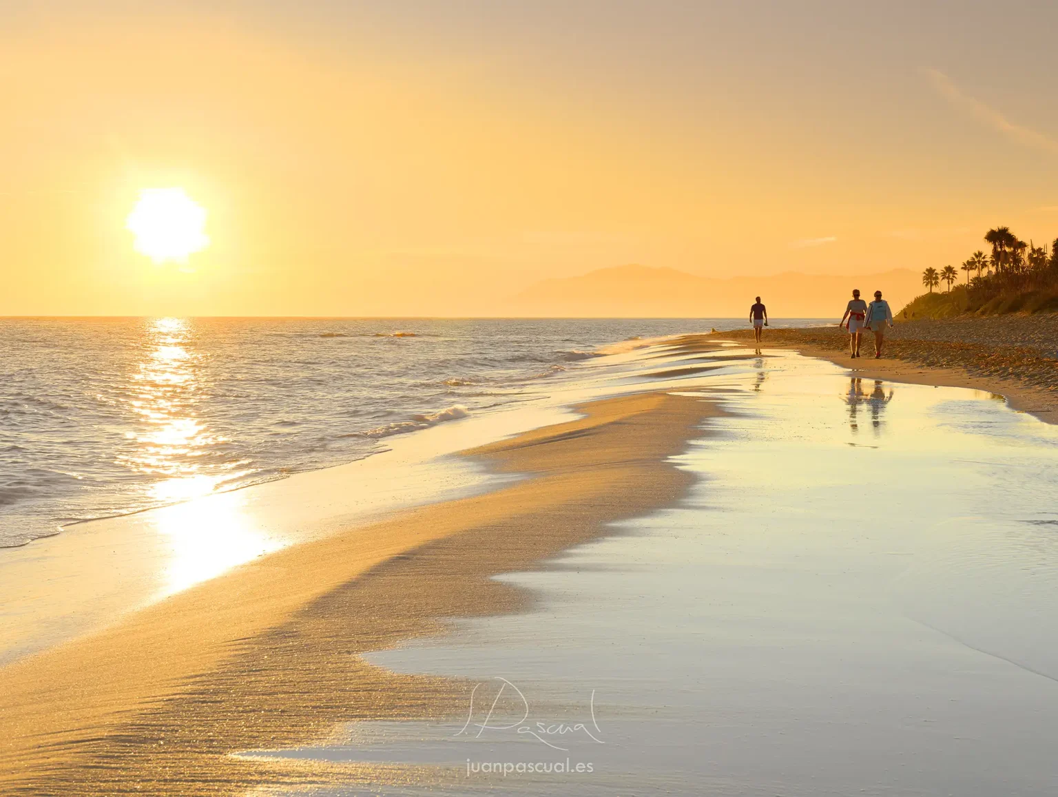 Atardecer en playa de Artola Cabopino en Marbella. Personas paseando junto al mar. Tonos amarillos y naranjas. Imagen relajante. Fotógrafo de turismo Juan Pascual